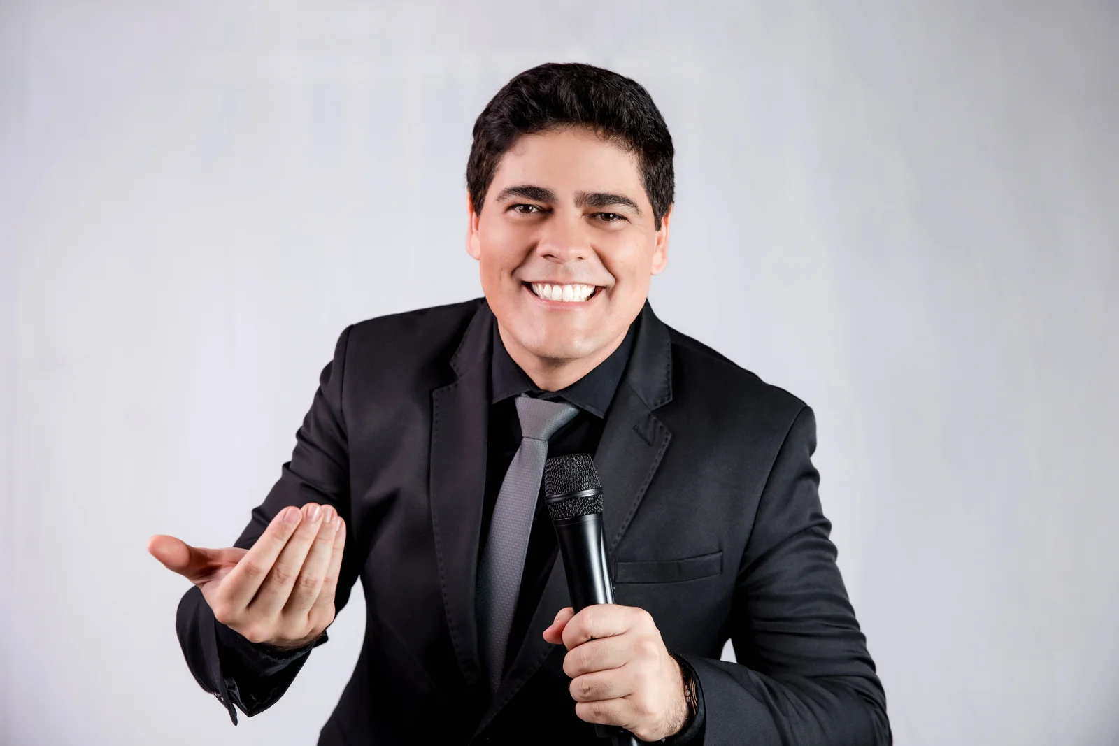 Matheus Pissolatti sorrindo, segurando microfone e gesticulando