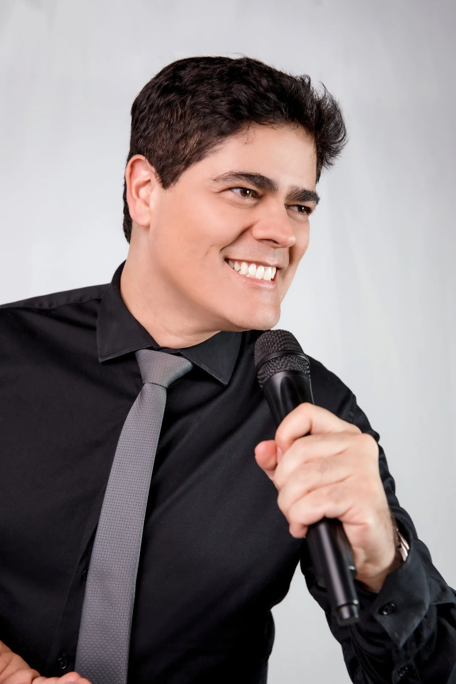Matheus Pissolatti de perfil, sorrindo, segurando microfone